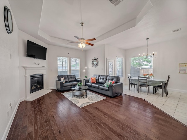 living room featuring a tray ceiling, visible vents, a glass covered fireplace, and wood finished floors