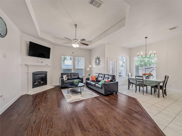 living area featuring visible vents, a glass covered fireplace, wood finished floors, and a raised ceiling