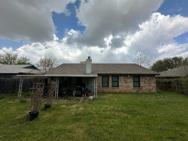 back of property with fence, a lawn, brick siding, an attached carport, and a chimney