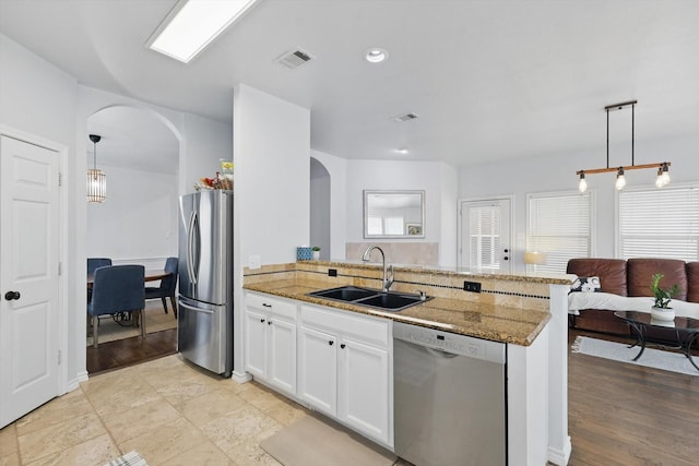 3505 Mustang Dr, Denton, TX 76210 - kitchen featuring appliances with stainless steel finishes, arched walkways, a sink, a peninsula, and light stone countertops