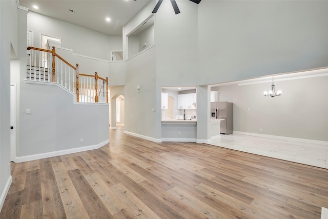10 Monticello Ct, Mansfield, TX 76063 - unfurnished living room featuring a chandelier, light wood-style floors, a ceiling fan, arched walkways, and a towering ceiling