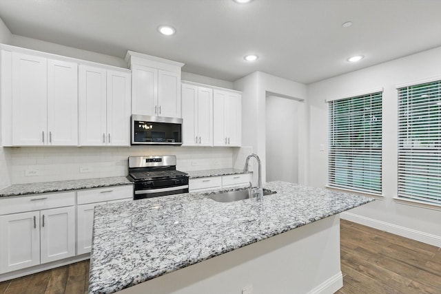 kitchen featuring appliances with stainless steel finishes, a sink, baseboards, white cabinets, and backsplash