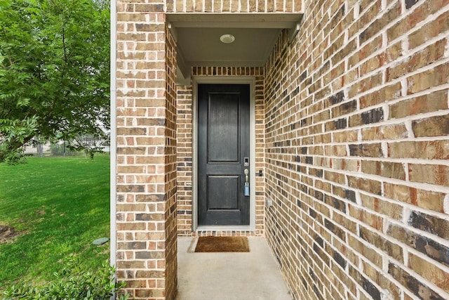 entrance to property with brick siding and a lawn