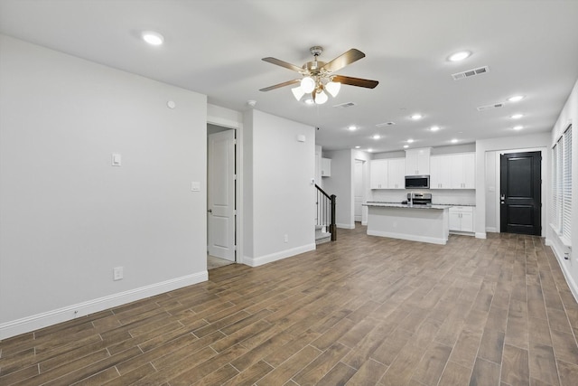 unfurnished living room featuring ceiling fan, baseboards, dark wood-style flooring, stairway, and recessed lighting
