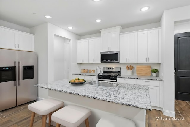 kitchen with appliances with stainless steel finishes, a sink, dark wood-type flooring, a breakfast bar area, and white cabinets