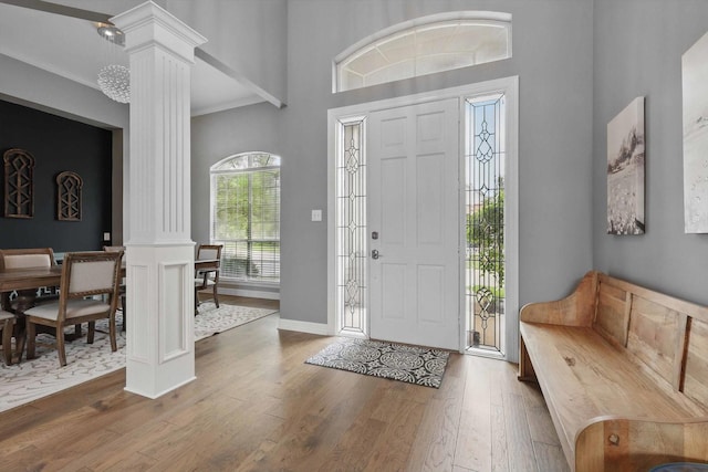 entrance foyer with ornate columns, wood finished floors, and a towering ceiling