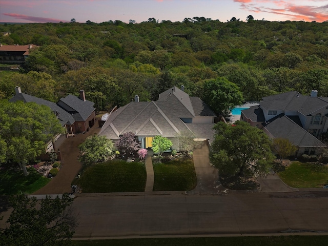 aerial view at dusk featuring a wooded view