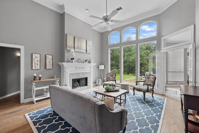 living area with visible vents, ornamental molding, a fireplace, a high ceiling, and a ceiling fan