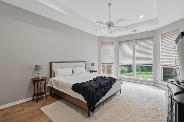 bedroom with visible vents, wood finished floors, baseboards, a tray ceiling, and recessed lighting