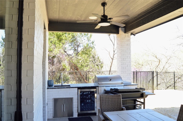 view of patio featuring a sink, fence, beverage cooler, exterior kitchen, and ceiling fan