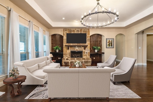living area with an inviting chandelier, arched walkways, baseboards, a fireplace, and dark wood-style flooring