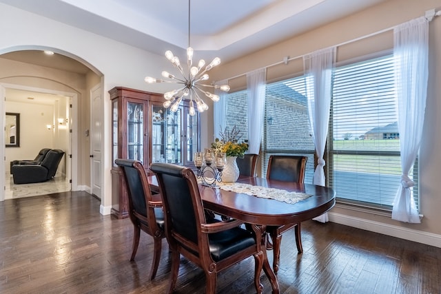 dining area featuring a tray ceiling, arched walkways, baseboards, an inviting chandelier, and wood finished floors