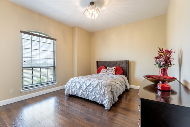 bedroom with an inviting chandelier, dark wood-style floors, and baseboards