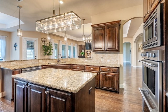 kitchen featuring light wood finished floors, a sink, arched walkways, tasteful backsplash, and appliances with stainless steel finishes