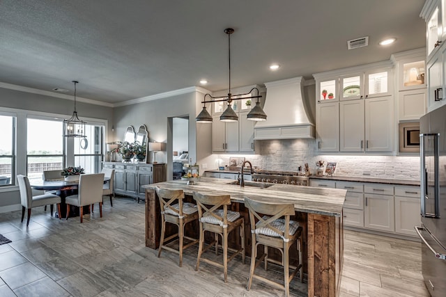 kitchen with a sink, tasteful backsplash, appliances with stainless steel finishes, custom exhaust hood, and visible vents