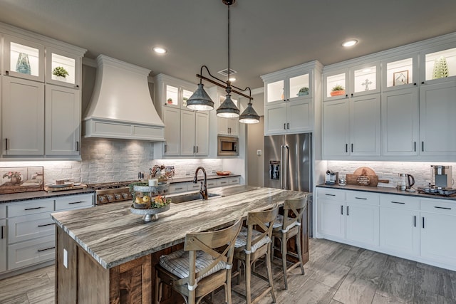kitchen with a kitchen breakfast bar, stainless steel appliances, a center island with sink, a sink, and custom exhaust hood