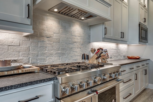 kitchen with custom exhaust hood, dark countertops, appliances with stainless steel finishes, light wood-type flooring, and backsplash