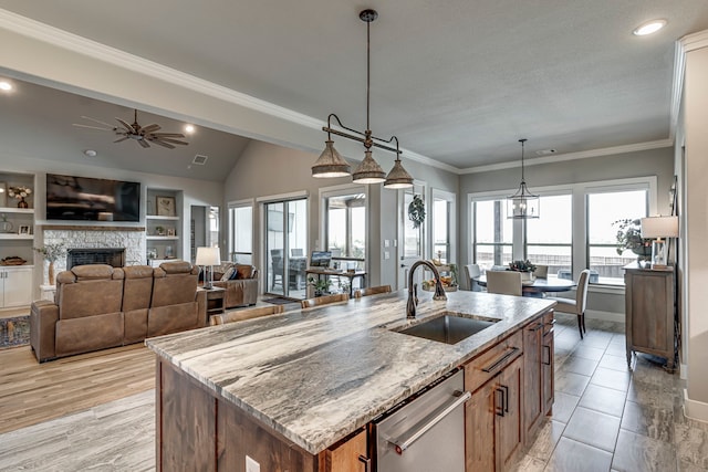 kitchen featuring stainless steel dishwasher, a center island with sink, a sink, light stone counters, and ceiling fan