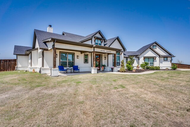 view of front facade featuring a chimney, fence, a front lawn, a shingled roof, and a patio area