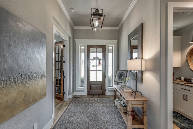 foyer with light wood-type flooring, visible vents, a textured wall, and ornamental molding