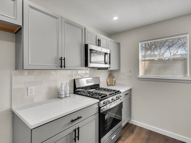 kitchen with dark wood-style flooring, gray cabinets, stainless steel appliances, baseboards, and backsplash