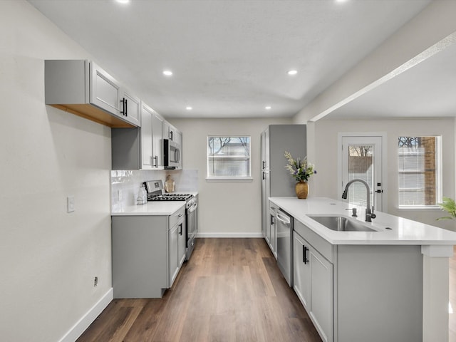kitchen with appliances with stainless steel finishes, a sink, baseboards, a peninsula, and dark wood-style floors