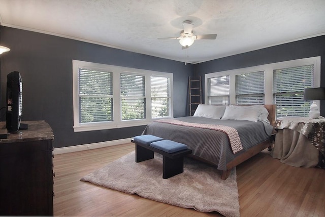 bedroom with light wood finished floors, baseboards, crown molding, and a ceiling fan