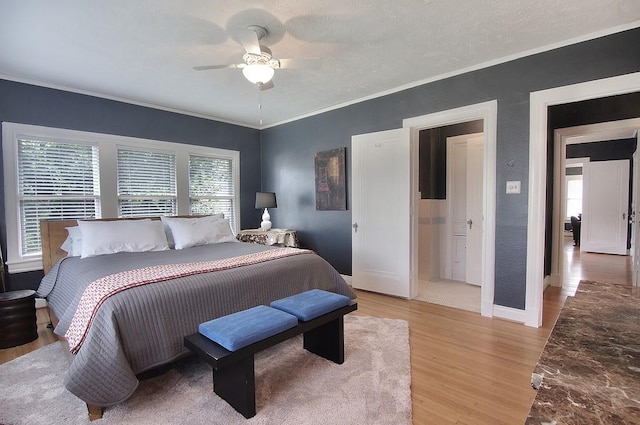 bedroom with ornamental molding, light wood-style flooring, baseboards, ceiling fan, and a textured wall