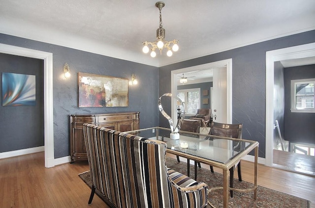 dining space with a textured wall, baseboards, wood finished floors, and a chandelier