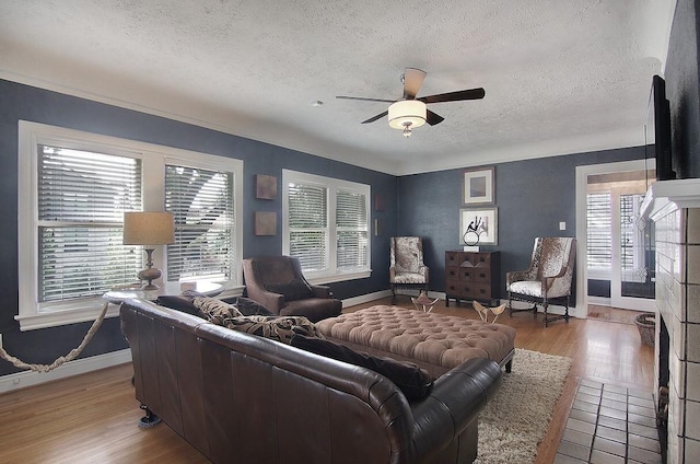 living area featuring baseboards, light wood-style floors, ceiling fan, and a textured ceiling