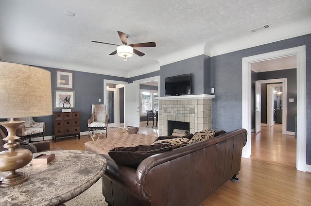 living room with a textured ceiling, visible vents, ceiling fan, wood finished floors, and a tiled fireplace