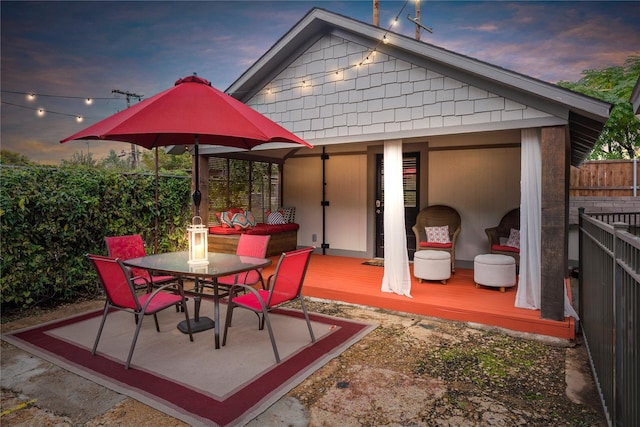 patio terrace at dusk with fence, outdoor dining space, and a deck