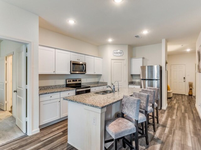 5665 Brownstone Ln, Fort Worth, TX 76036 - kitchen with white cabinets, a kitchen breakfast bar, stainless steel appliances, wood finished floors, and a sink