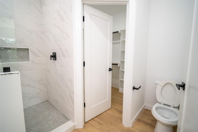 bathroom with baseboards, wood finished floors, a tile shower, and toilet