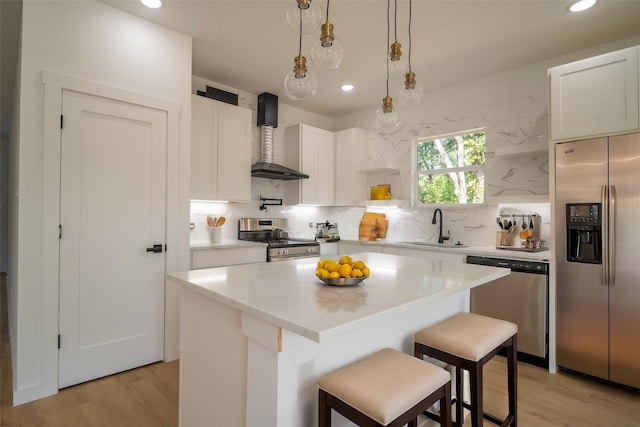 kitchen featuring a sink, wall chimney exhaust hood, appliances with stainless steel finishes, and light wood-style flooring