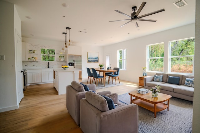 living room with visible vents, a ceiling fan, light wood-style floors, and baseboards