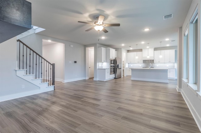 unfurnished living room with visible vents, wood finished floors, ceiling fan, and a sink