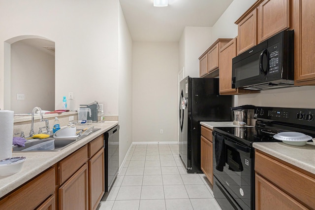 kitchen with a sink, black appliances, light tile patterned floors, arched walkways, and light countertops