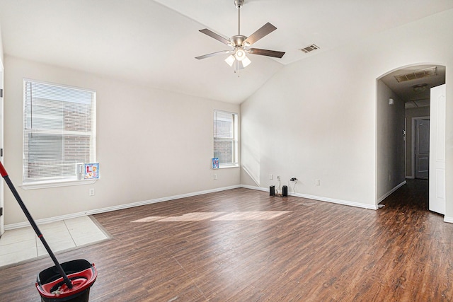 empty room featuring arched walkways, lofted ceiling, wood finished floors, and plenty of natural light