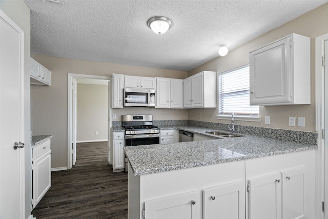 kitchen featuring a peninsula, a sink, dark wood-style flooring, white cabinetry, and appliances with stainless steel finishes
