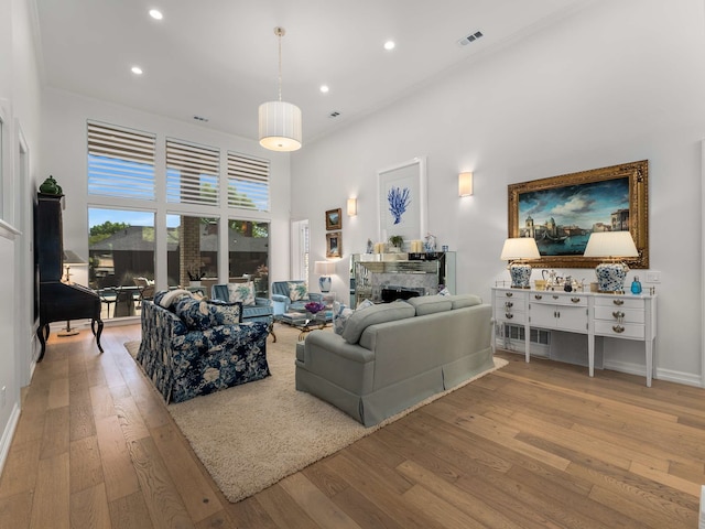 living area with a towering ceiling, visible vents, a fireplace, wood-type flooring, and recessed lighting