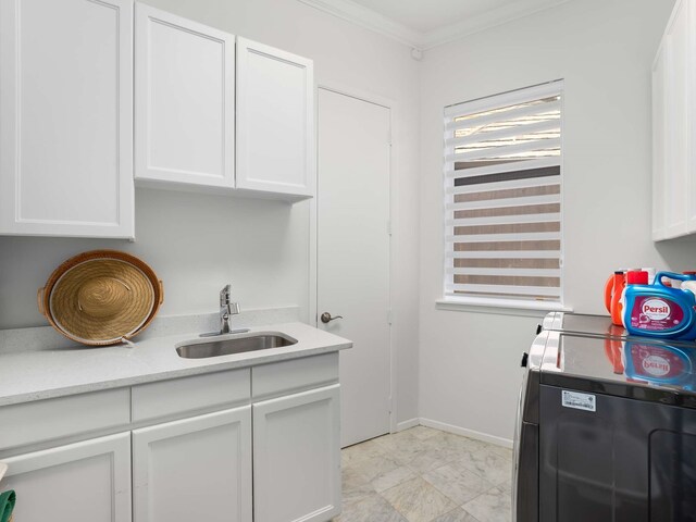 washroom featuring crown molding, washing machine and clothes dryer, cabinet space, a sink, and baseboards