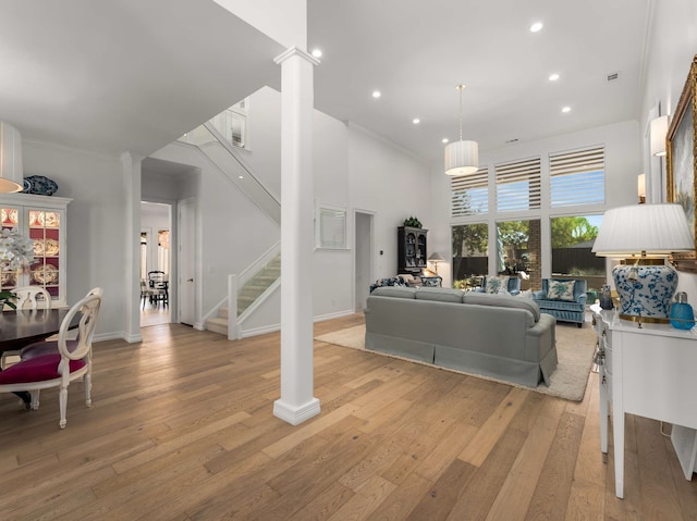living area with decorative columns, a towering ceiling, light wood-style floors, stairway, and recessed lighting
