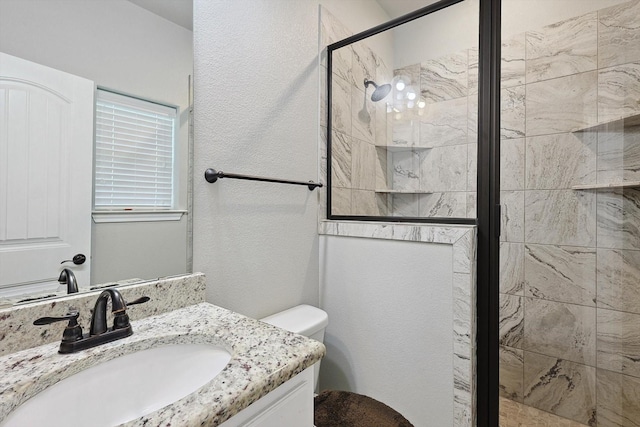 full bathroom featuring vanity, a textured wall, toilet, and a shower stall