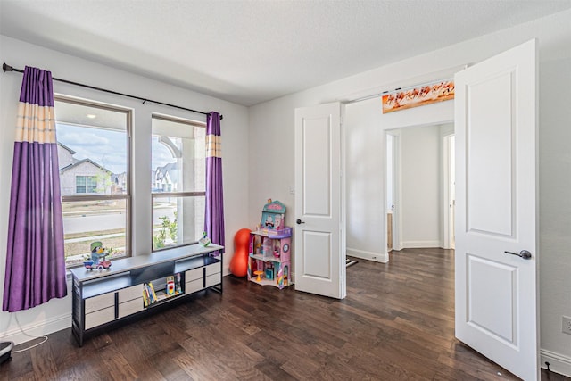 playroom featuring baseboards, dark wood-type flooring, and a textured ceiling