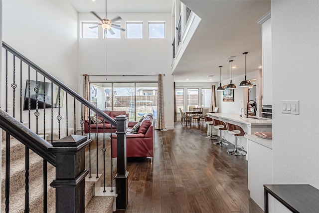 interior space with dark wood-type flooring, a towering ceiling, stairway, and a ceiling fan