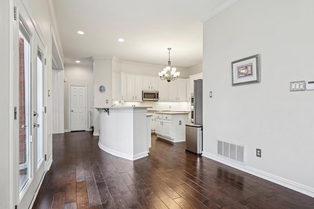 4516 Chesterwood Dr, Plano, TX 75093 - kitchen featuring stainless steel appliances, a chandelier, a peninsula, dark wood finished floors, and white cabinetry