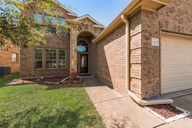 doorway to property featuring an attached garage, central AC, brick siding, and a yard