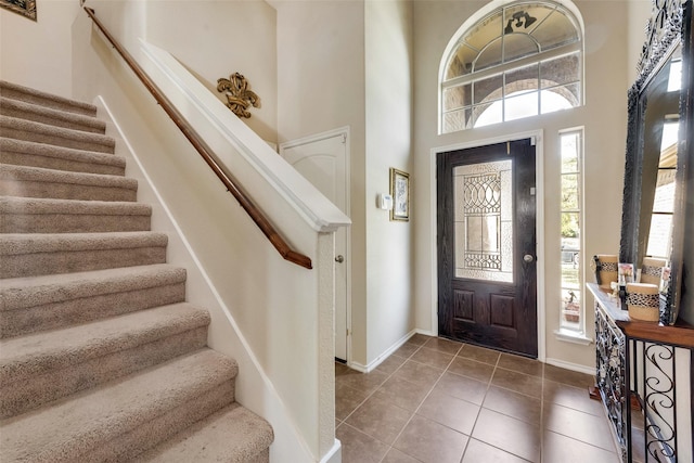 tiled entryway featuring baseboards, a wealth of natural light, a high ceiling, and stairway