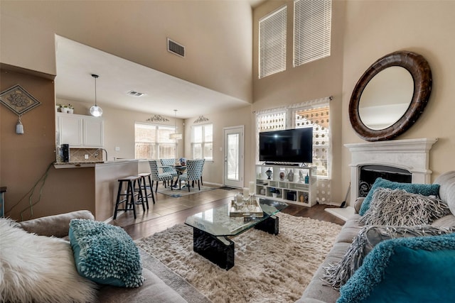 living room with visible vents, wood finished floors, a fireplace with raised hearth, and a towering ceiling